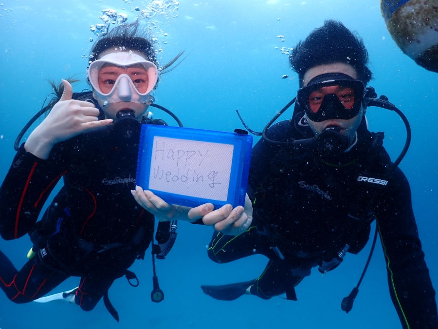 ハワイの海中で「Happy Wedding」のメッセージボードを持つ新婚カップルの体験ダイバー
