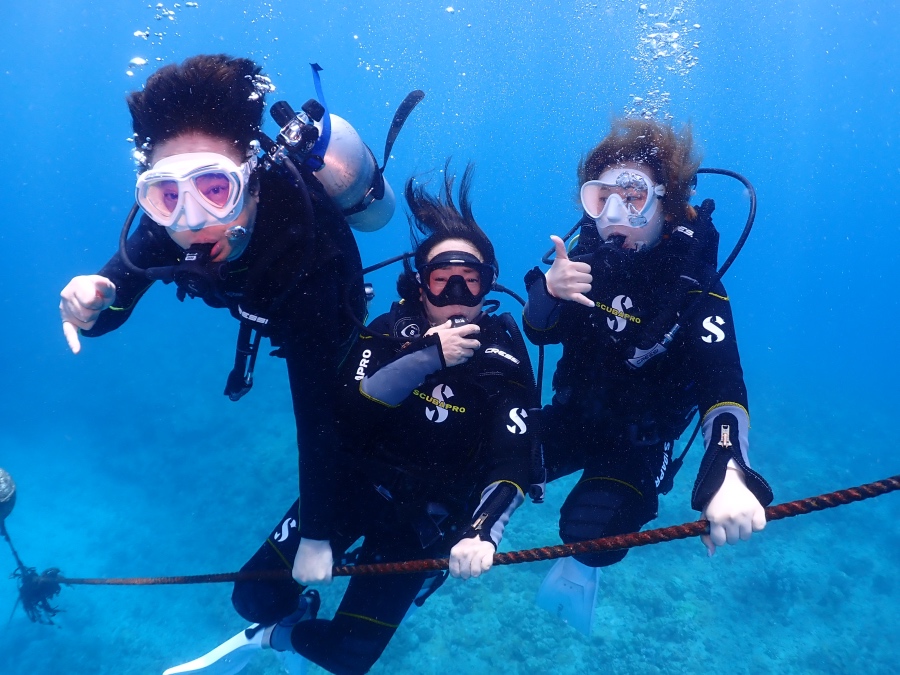 ハワイの海で潜降ロープにつかまり笑顔を見せる3名のダイバー