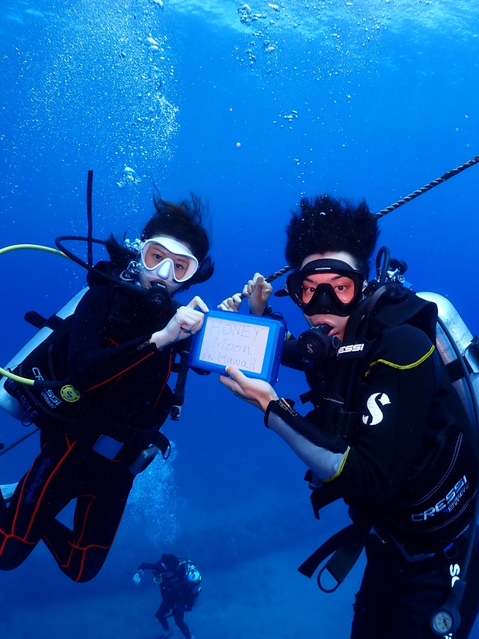 ハワイの海でハネムーンの記念ボードを持ってFUNダイビングを楽しむご夫婦