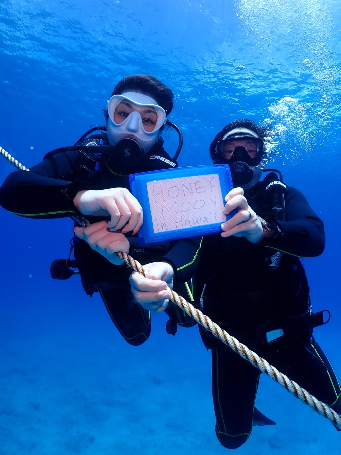ハワイの海でハネムーンのボードを持って体験ダイビングを楽しむご夫婦