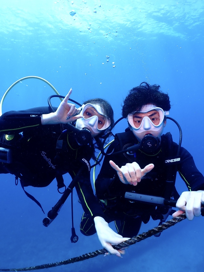 ハワイの海で潜降ロープをつかみアロハポーズをする体験ダイビングのカップル