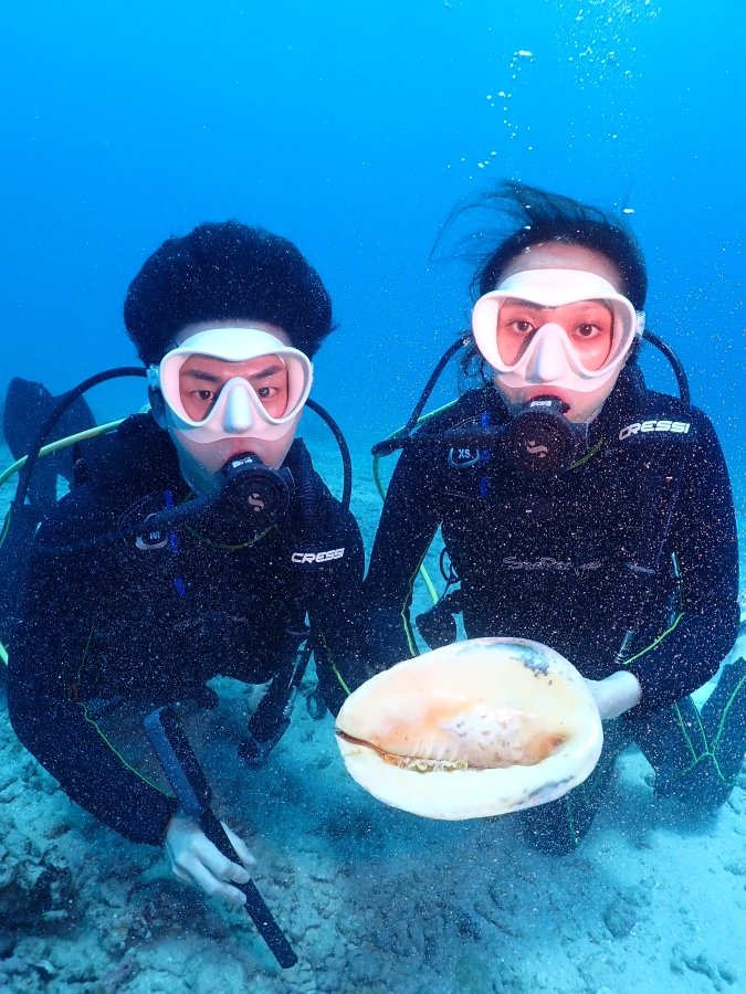 ハワイの海底で巨大なトウカムリの貝を持って笑顔を見せる体験ダイビングの二人