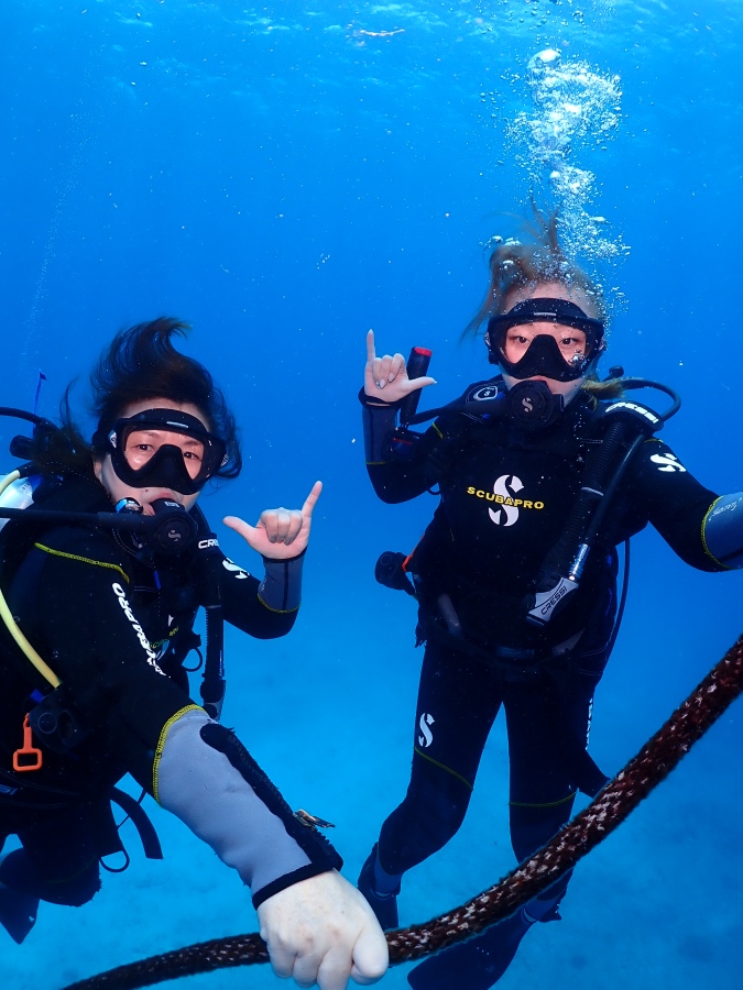 ハワイの透明度の高い海で潜降ロープをつかみシャカサインをする親子ダイバー