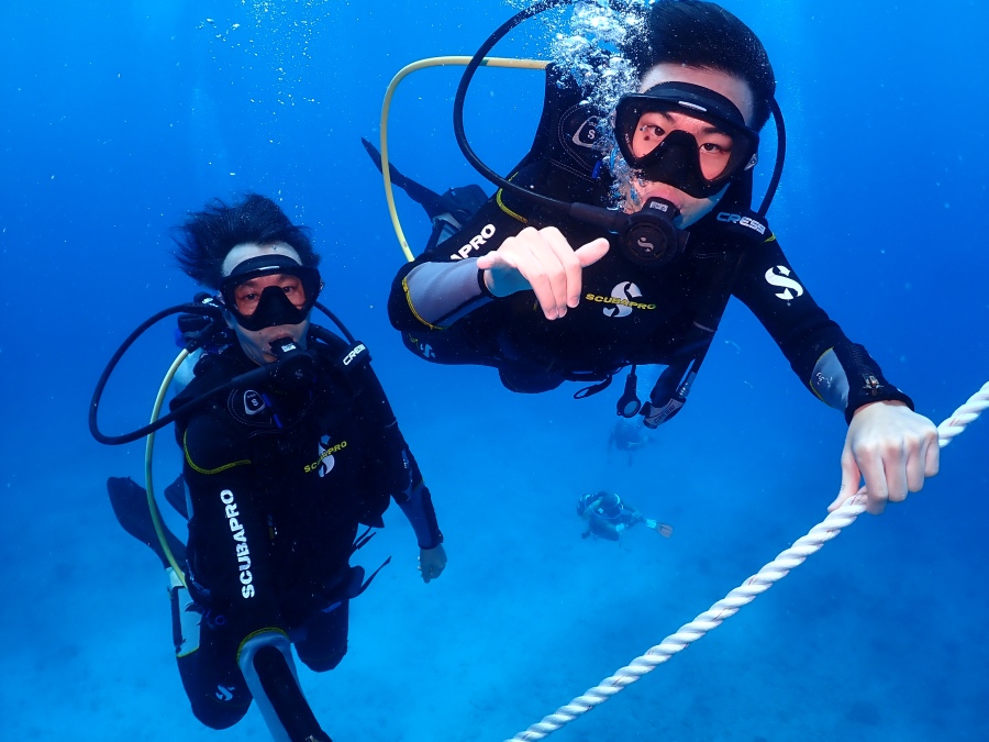 ハワイの透明度の高い海でロープをつかみリラックスして潜降する親子の体験ダイバー