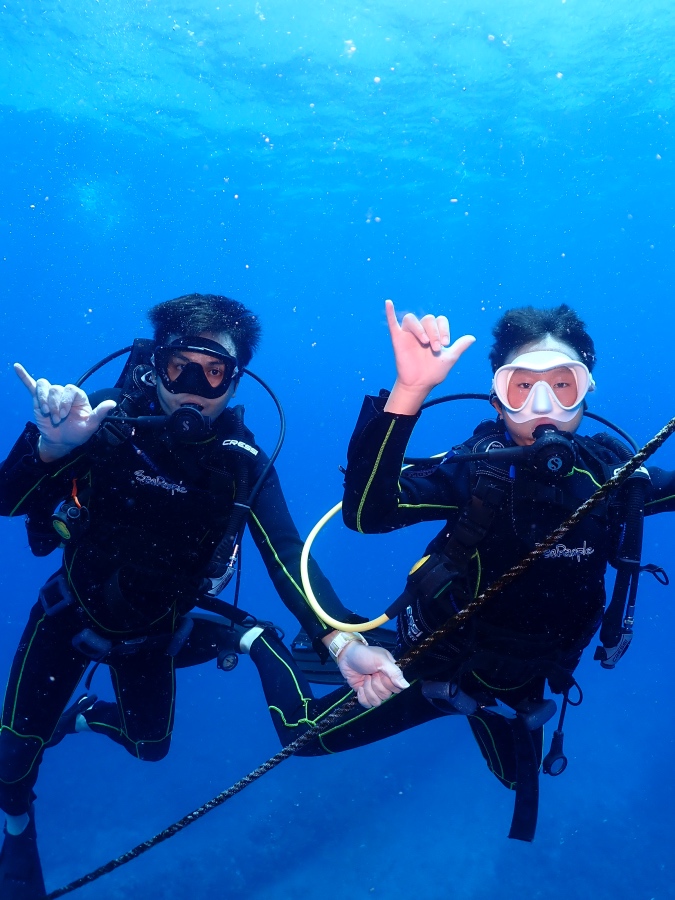 ハワイの透明な海で潜降ロープをつかみアロハポーズを決める親子ダイバー