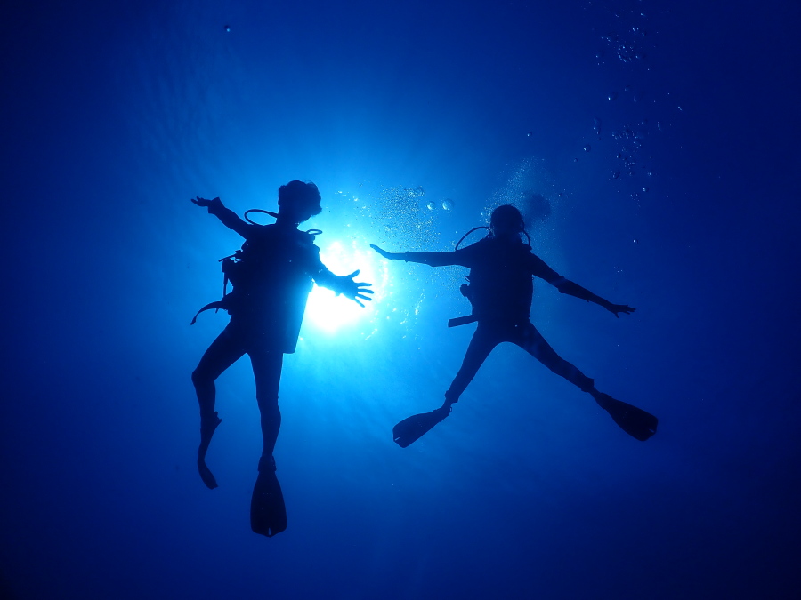 ハワイの眩しい太陽の光に向かって手を広げるダイバーの美しい水中シルエット