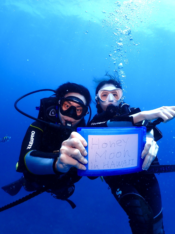 ハワイの海でHoney Moon in HAWAIIのメッセージボードを持ち微笑む新婚ご夫婦