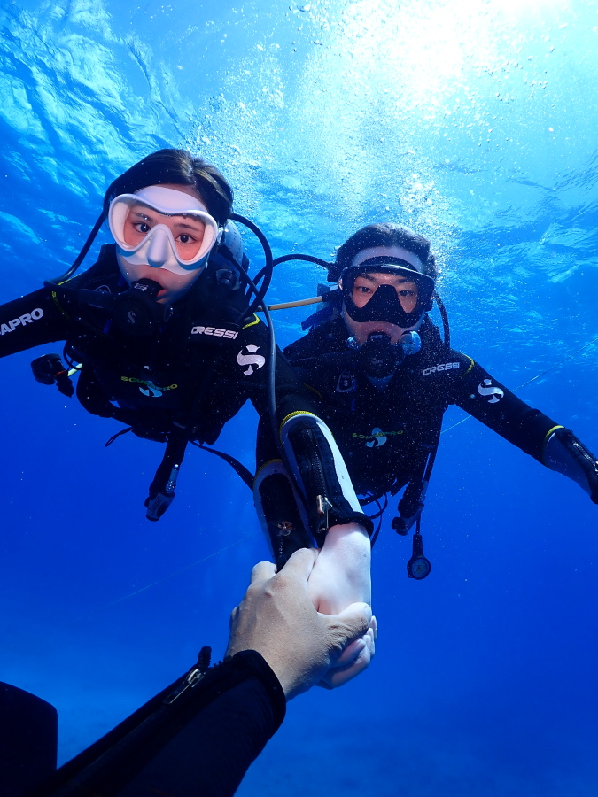 ハワイの青い海でガイドのサポートを受けながら手をつないで仲良く泳ぐ新婚カップル