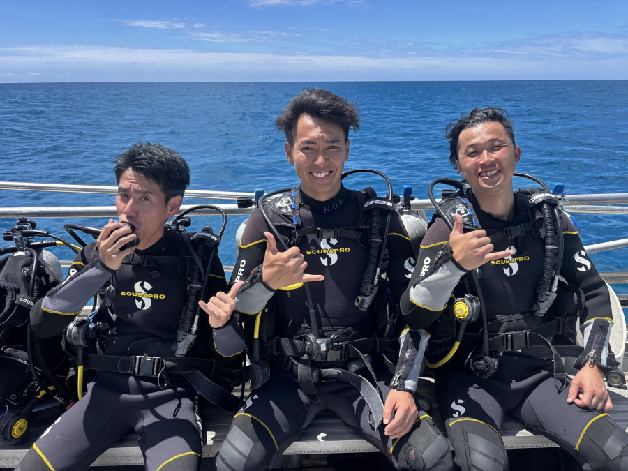 ハワイの青空のもとボート上でダイビング器材を装着し笑顔でシャカサインを決める男性グループ3名