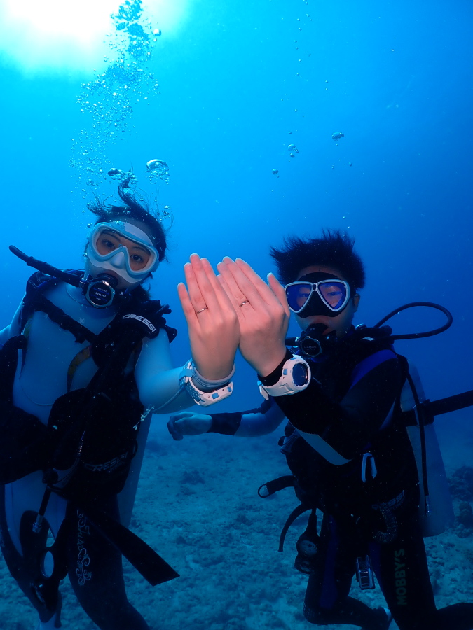 ハワイのクリアな青い海の中で薬指に輝く結婚指輪を重ねて並べる新婚カップル